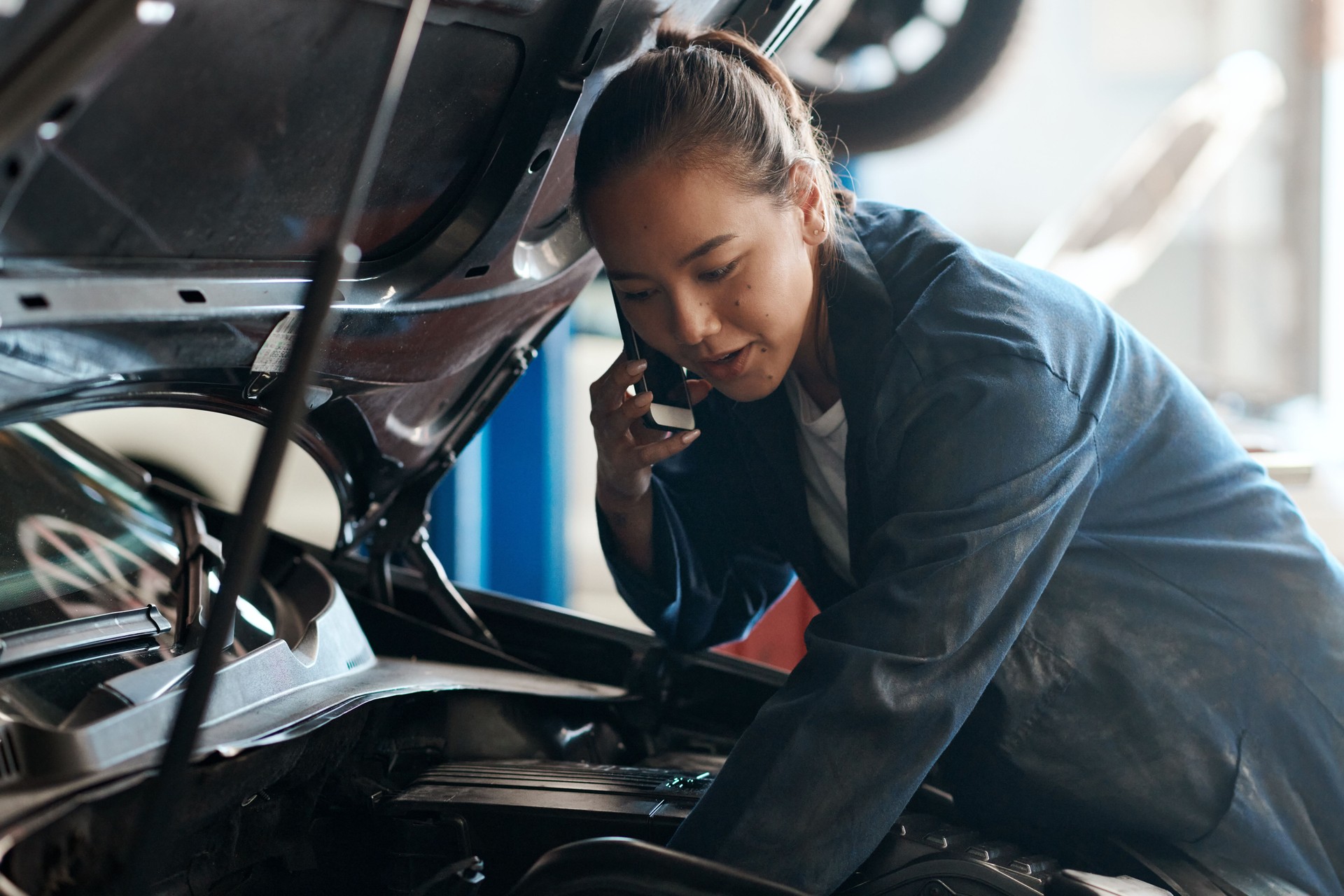 Aufnahme einer Mechanikerin, die auf ihrem Handy spricht, während sie in einer Autowerkstatt arbeitet