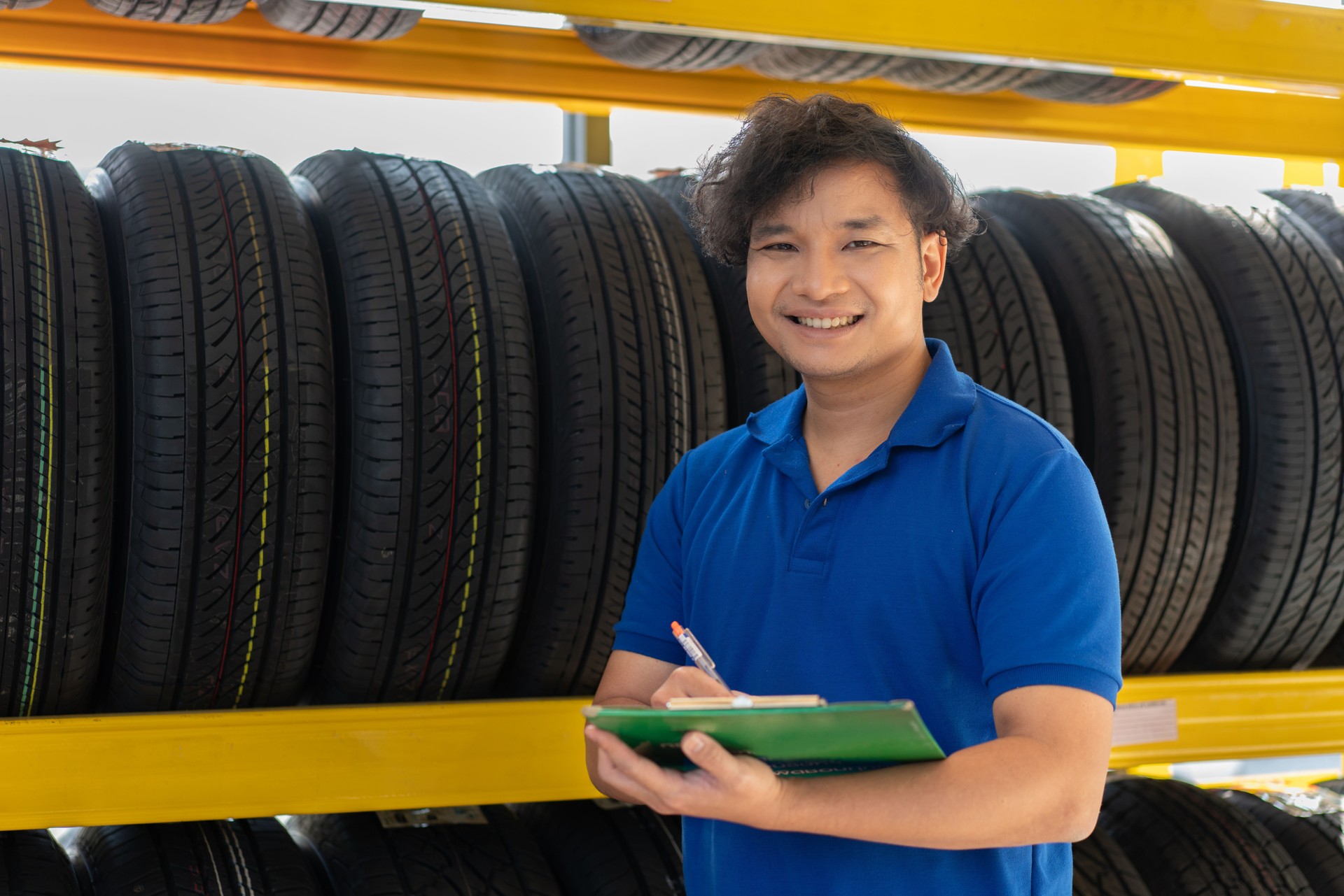 Porträt eines asiatischen männlichen Technikers, der das Rad neuer Reifen im Regal in der Autowerkstatt und im Autoreparaturservice überprüft